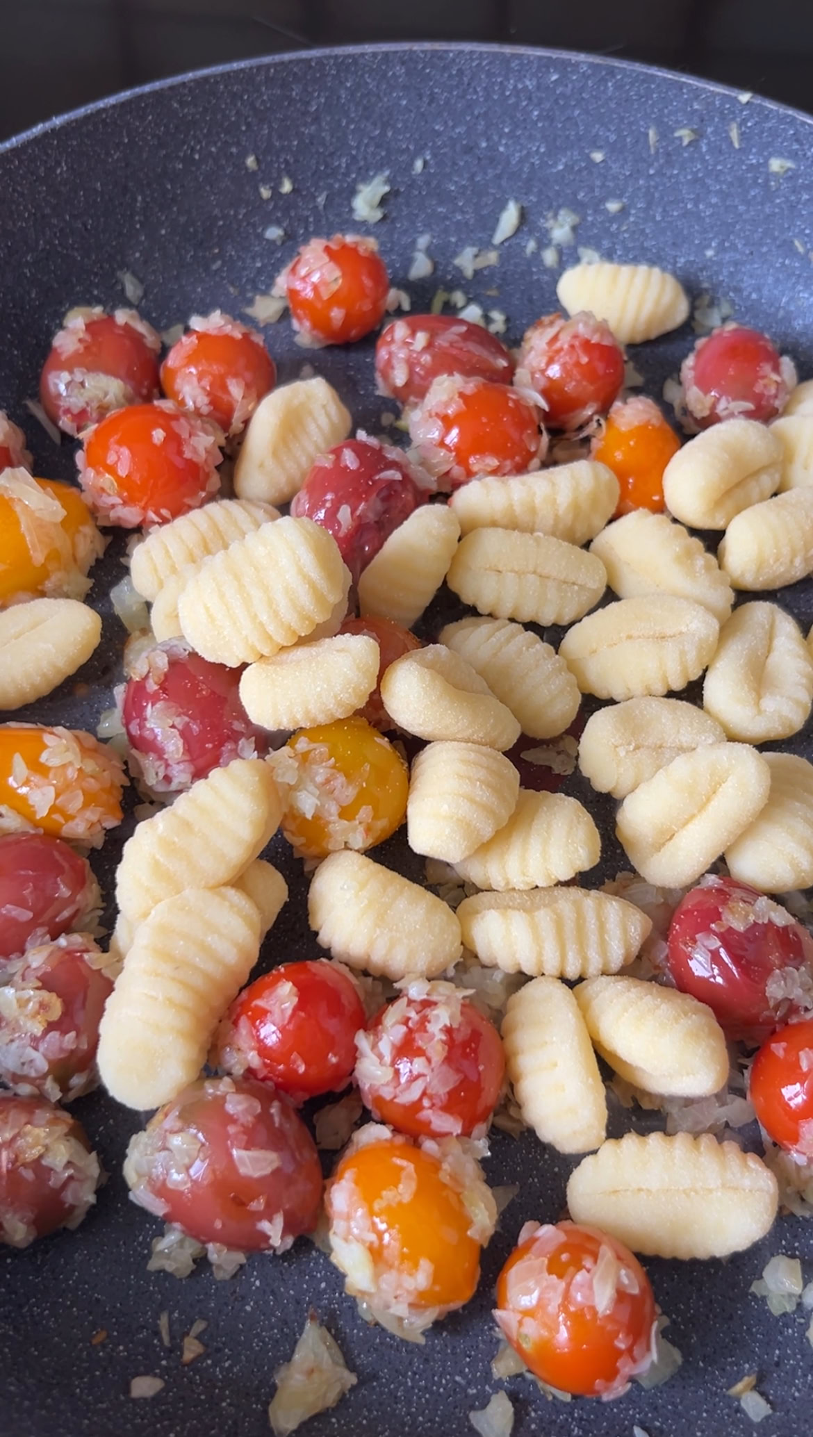 Uncooked gnocchi added to the pan of garlic, onion and cherry tomatoes.