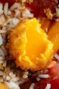 Fried egg yolk cut in half and opened, with a runny inside and crispy golden outside, all in a bowl of rice salad with tomatoes.