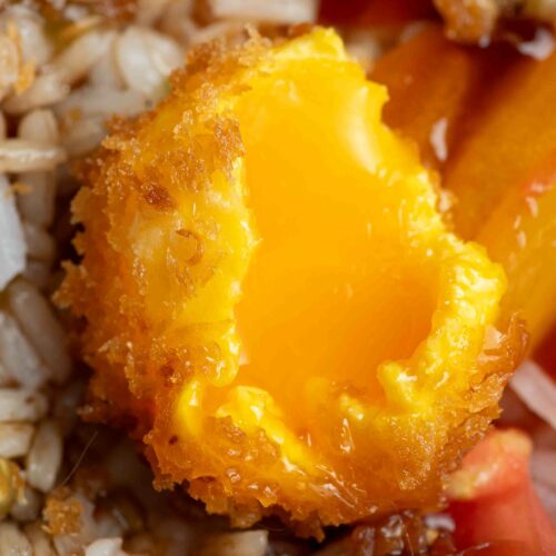 Fried egg yolk cut in half and opened, with a runny inside and crispy golden outside, all in a bowl of rice salad with tomatoes.