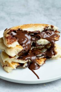 Four half-pancakes stacked on top of each other and dripping with runny Nutella.