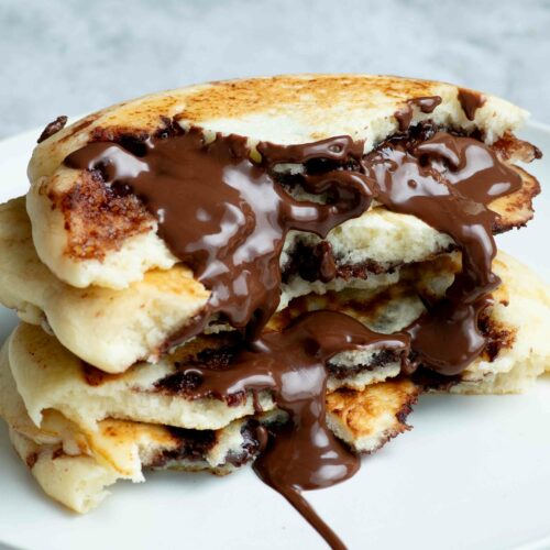 Four half-pancakes stacked on top of each other and dripping with runny Nutella.