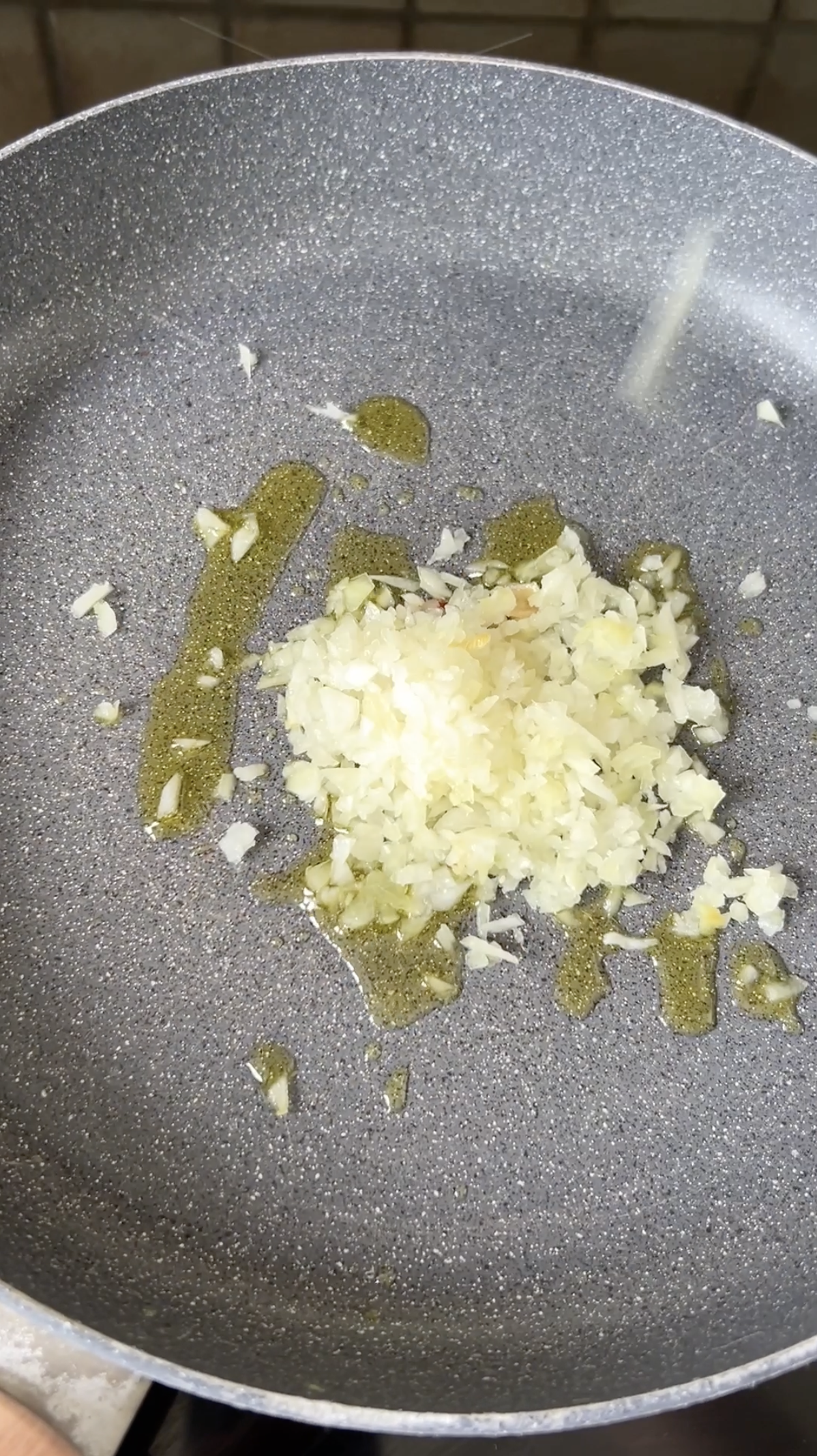 Oignon finement émincé dans une poêle grise avec de l'huile d'olive.