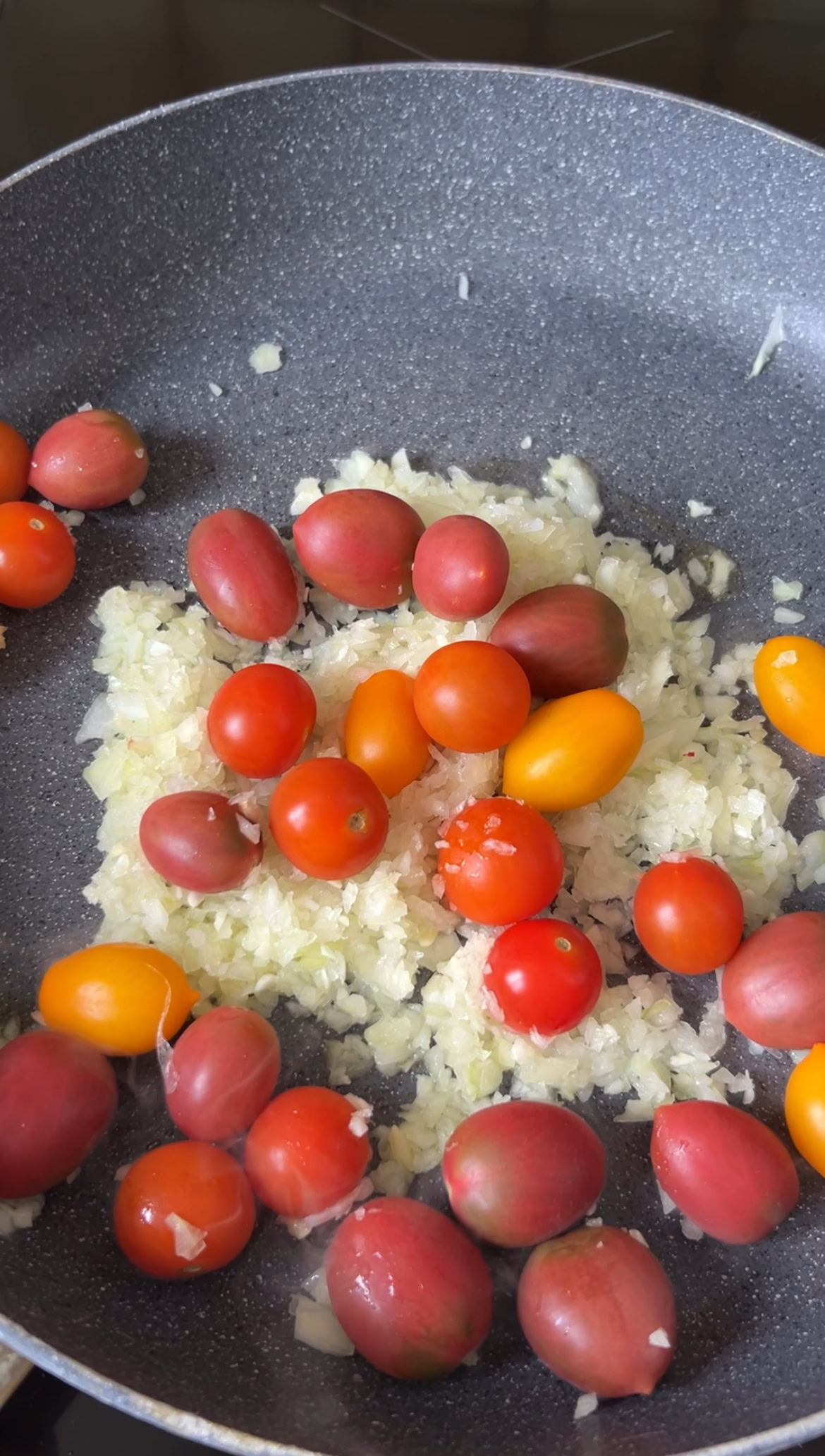Minced onion and garlic in a frying pan with cherry tomatoes.