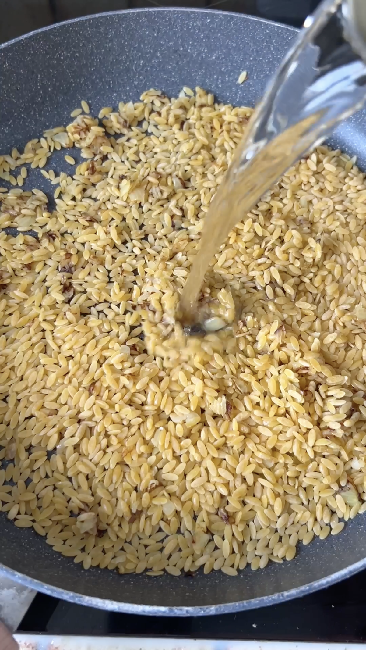 Orzo pasta cooking in the pan with stock falling in.