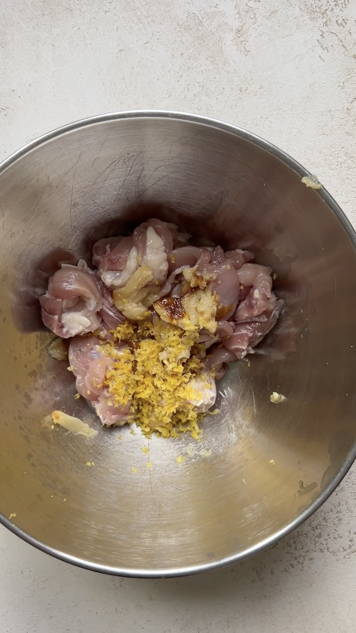 Chicken pieces and lemon zest in a stainless steel bowl.