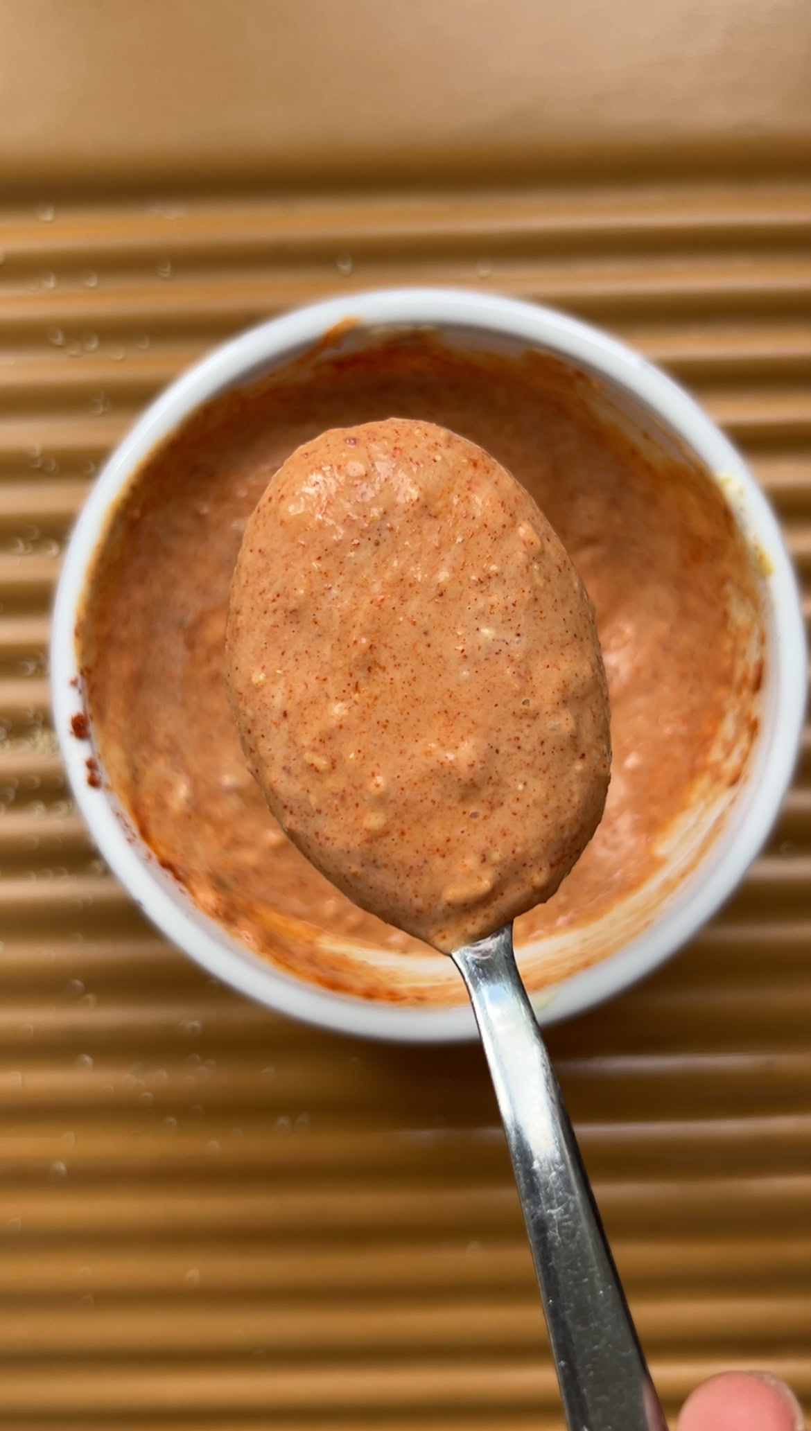 Sauce mélangée et un peu de sauce tenue par une cuillère à café, au dessus du bol.