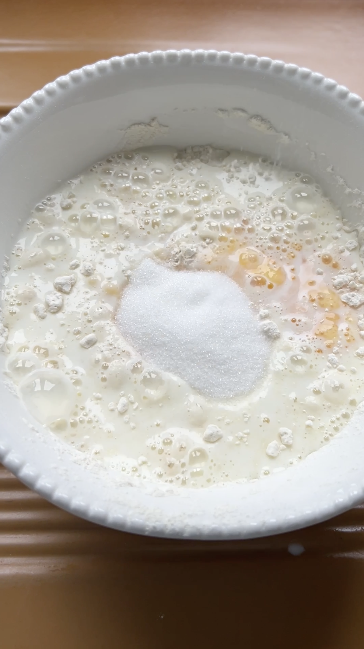 Sucre ajouté au bol blanc de farine, de lait et d'œuf battu.