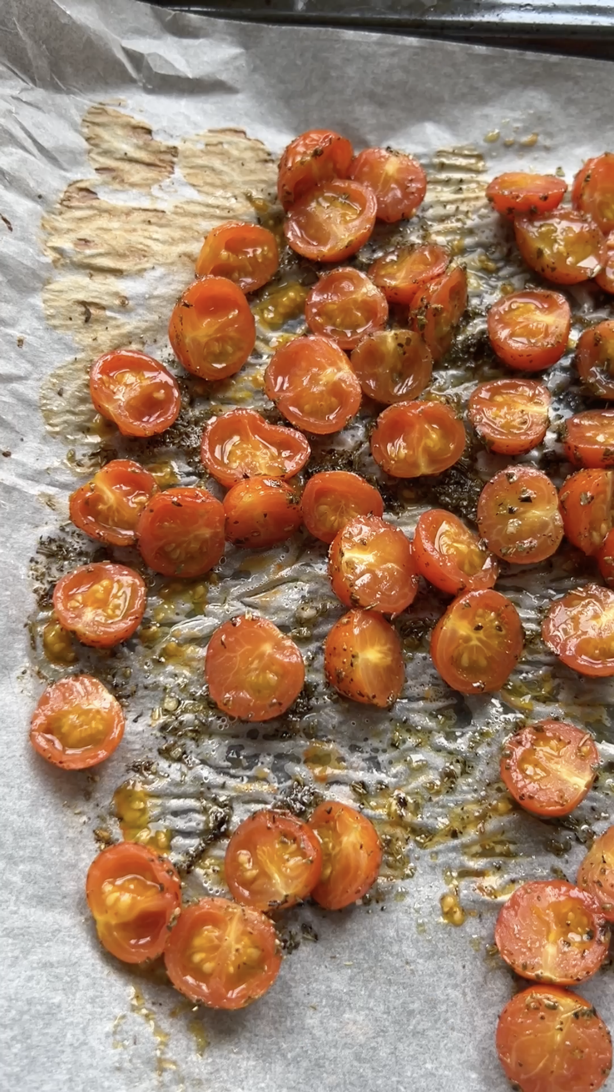 Cherry tomatoes cut in half, halfway through baking, on a sheet of baking paper.
