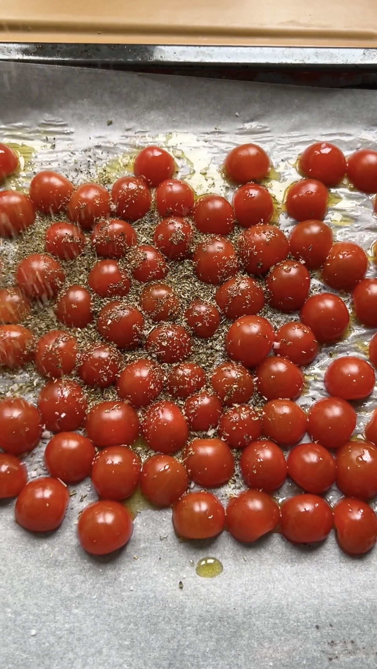 Tomates cerises coupées en deux et posées sur une feuille de papier cuisson, avec de l'huile d'olive et de l'origan.