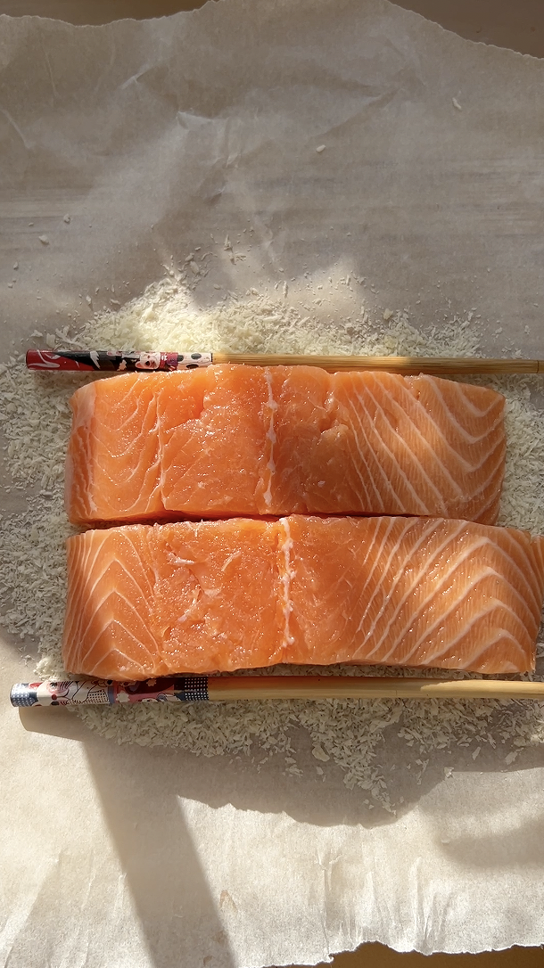 Two salmon fillets between two chopsticks, on a sheet of parchment paper with breadcrumbs.