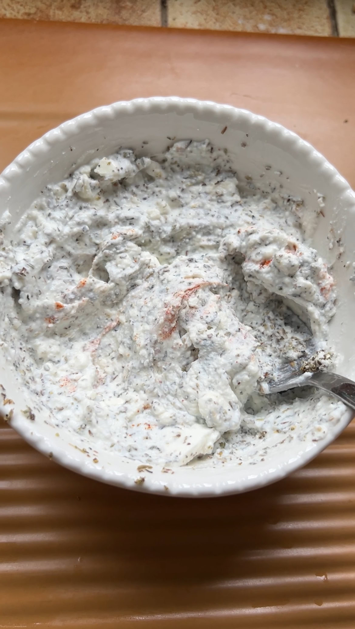 Feta, ricotta, oregano, thyme, lemon juice and cayenne pepper in a small white bowl, mixed with a tablespoon.