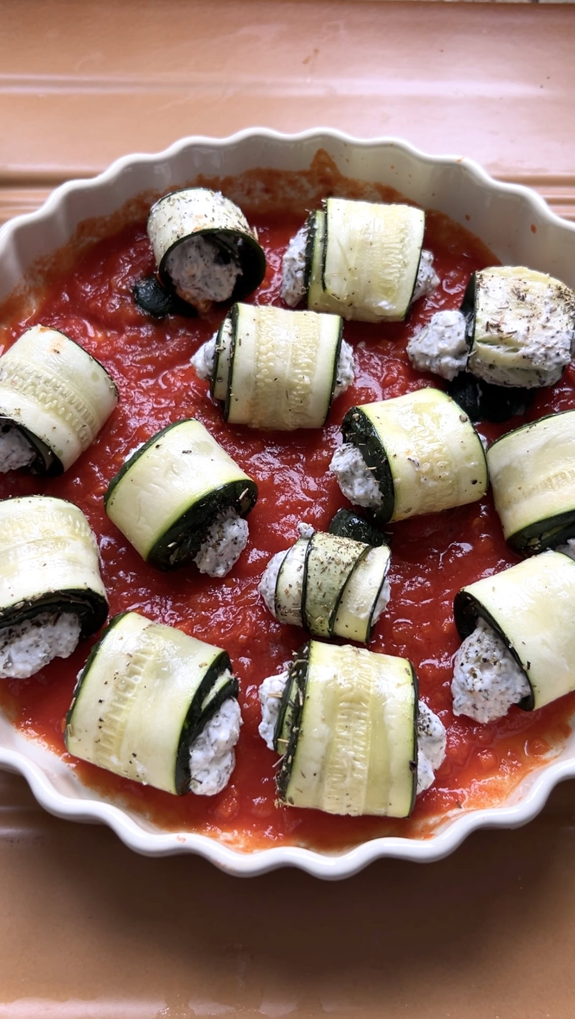 The zucchini involtini are placed in the large round dish of tomato sauce.