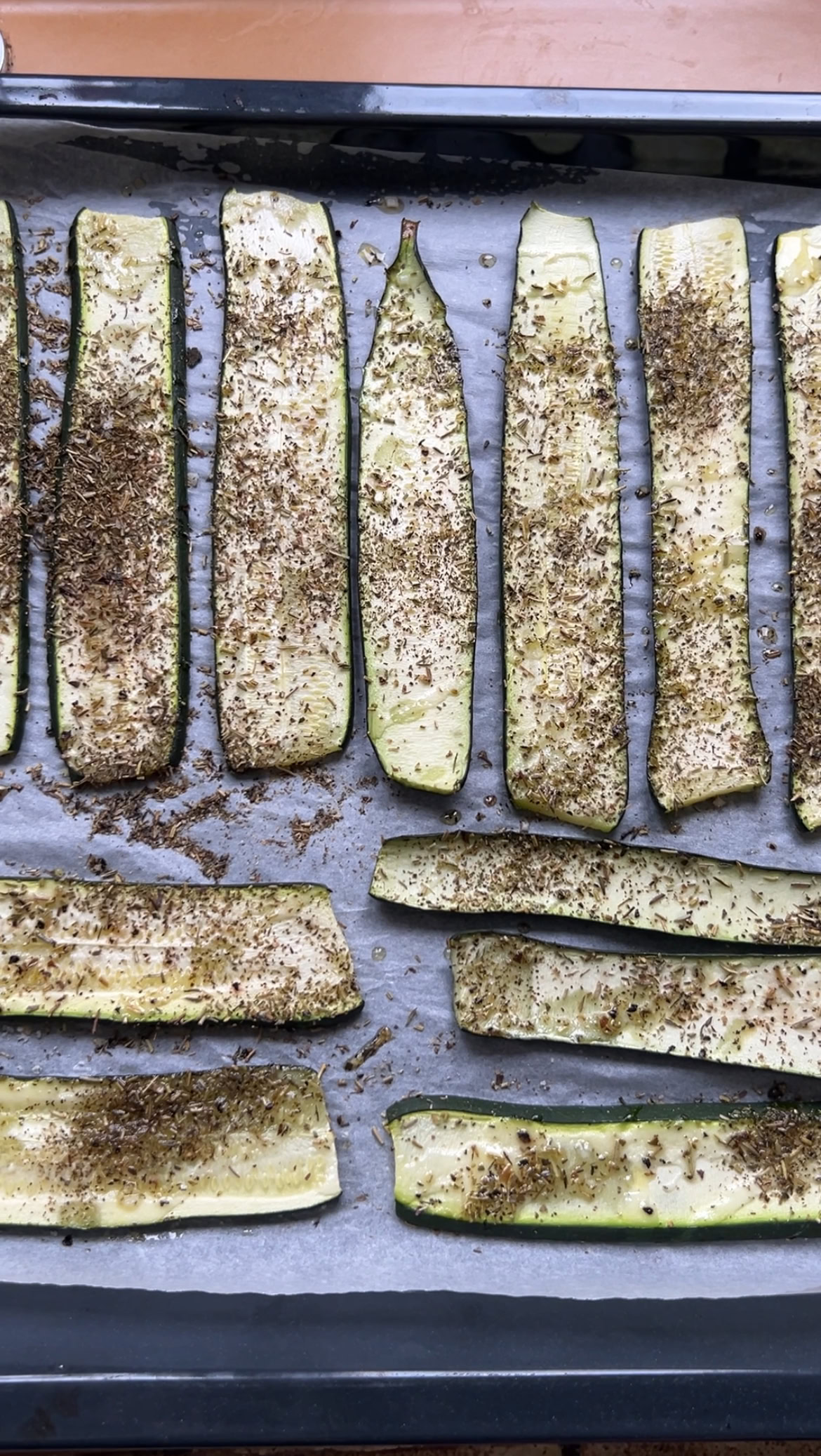 Lamelles de courgette assaisonnées, posées sur une plaque du four recouverte de papier cuisson, après leur cuisson.