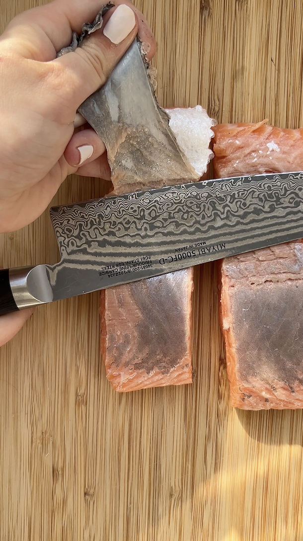 Hand holding a knife and removing the skin from one of the salmon fillets.
