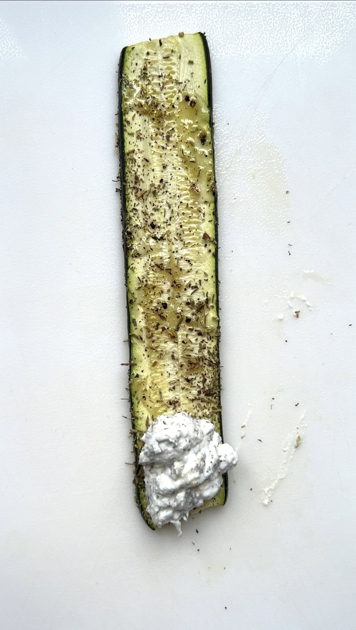 Un peu de garniture au fromage déposée sur une lamelle de courgette, posée sur une planche blanche.