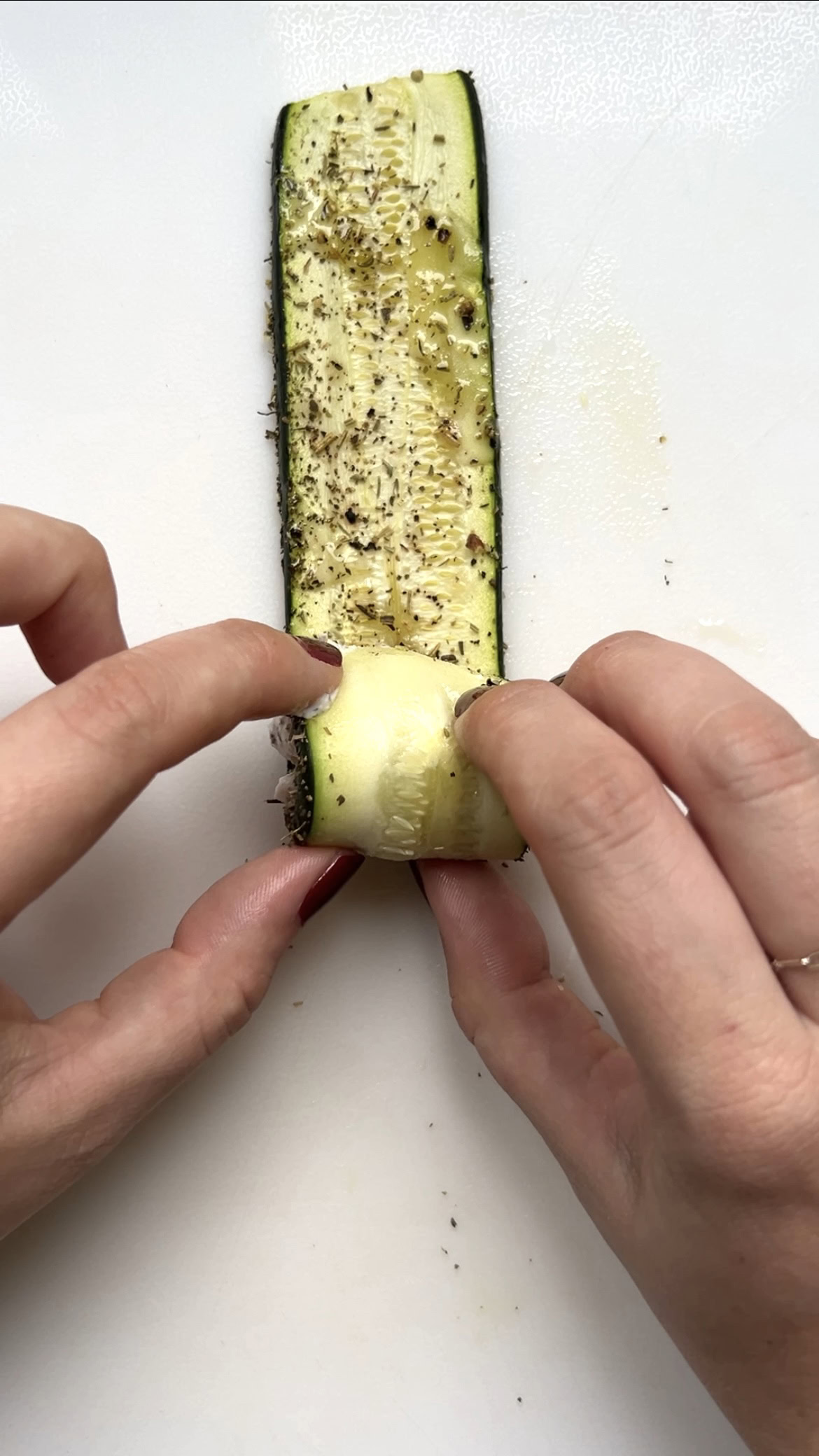 Two hands rolling the zucchini slice over itself.