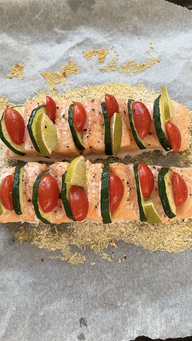 Two salmon fillet garnished with cherry tomato halves, zucchini strips and lime wedges, after baking.
