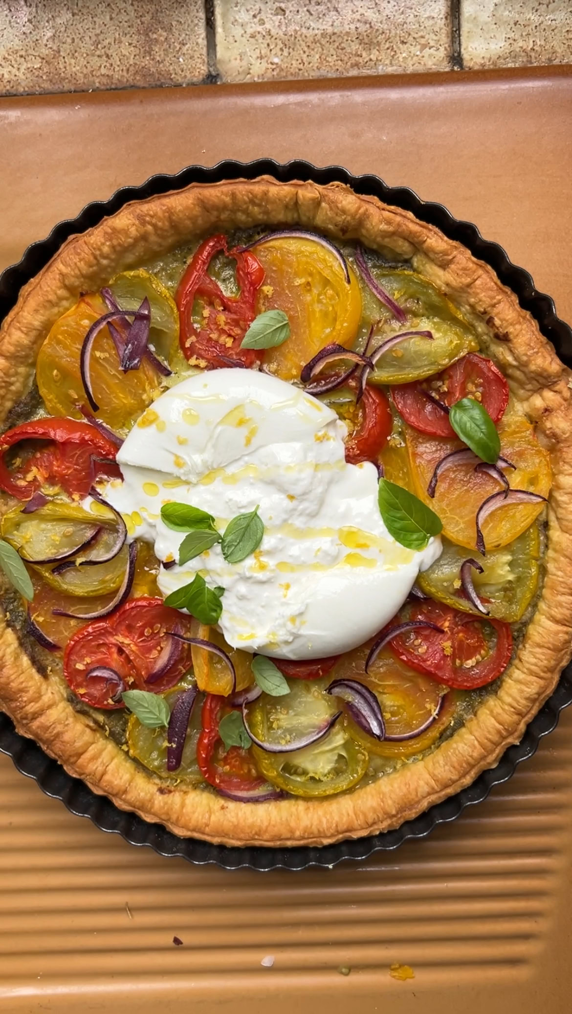 Burrata added to tomato tart, with a few fresh basil leaves and a drizzle of olive oil.