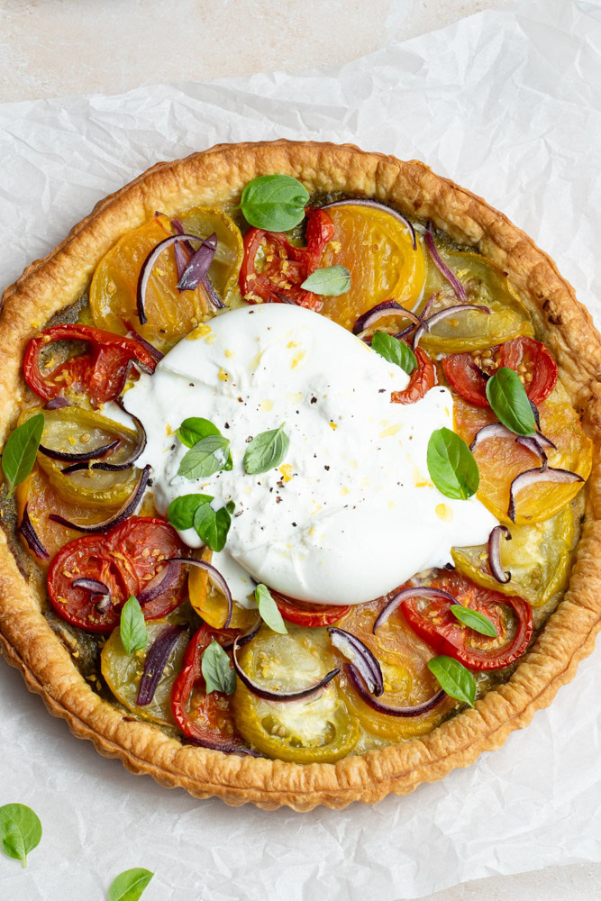 Multicolored tomato tart with a large burrata in the middle and several fresh basil leaves.
