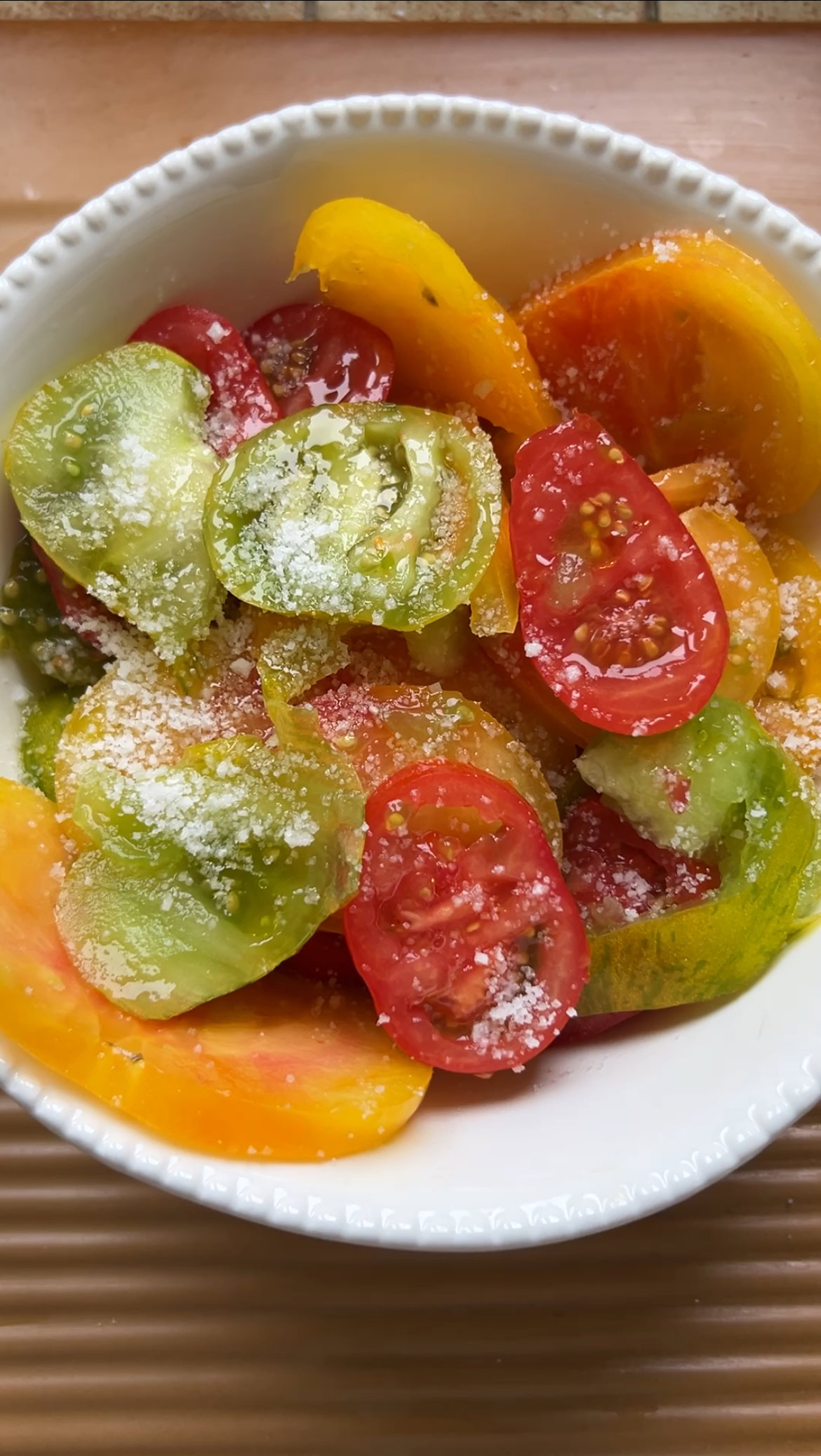 Sliced tomatoes in a large white bowl, with olive oil and sea salt.