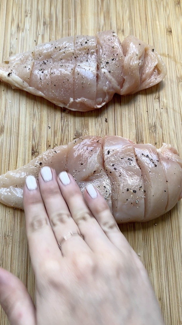 Une main qui masse le filet de poulet, avec du sel et du poivre.