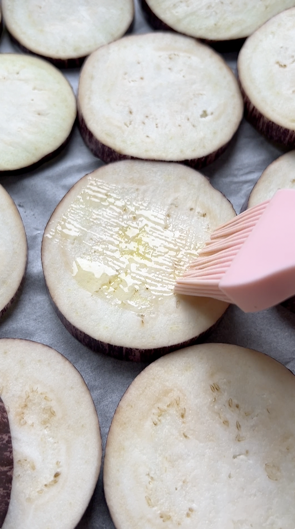 Lamelles d'aubergine badigeonnées d'huile d'olive par un pinceau en silicone rose.