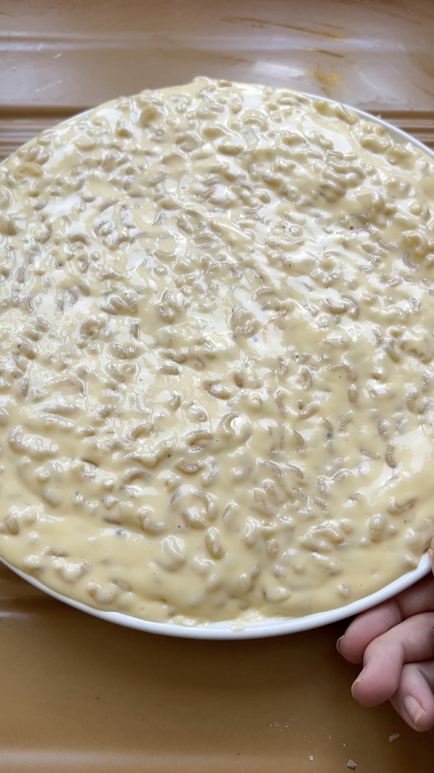 The mixture of pasta, cheese and béchamel sauce is spread out on a large white plate.