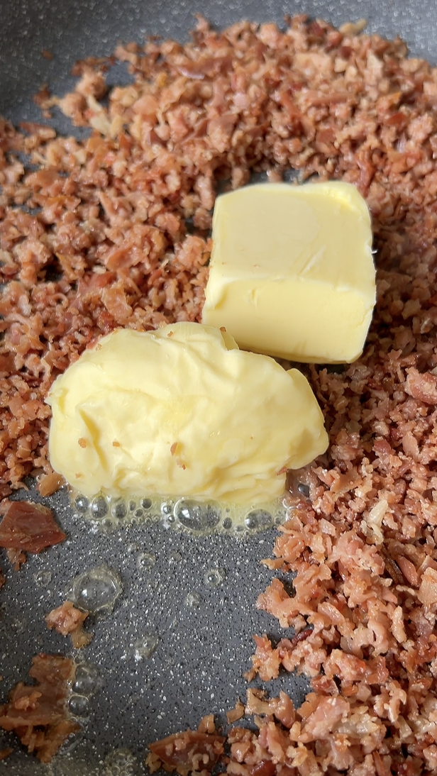 Deux morceaux de beurre rajoutés à la poêle de jambon Serrano haché, qui cuit.