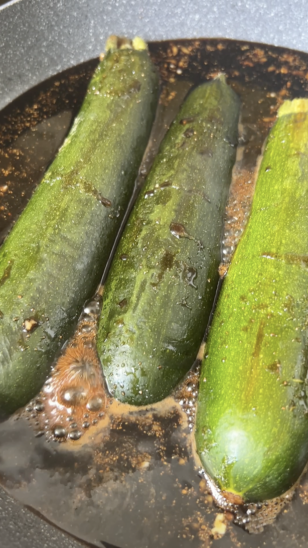 Four zucchini halves cooking in a large frying pan, with homemade Teriyaki sauce.