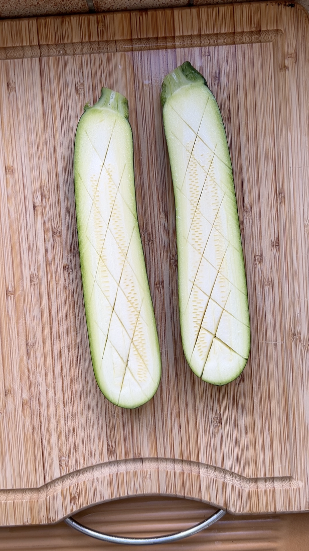 Deux demies courgettes sur une planche en bois, quadrillées.