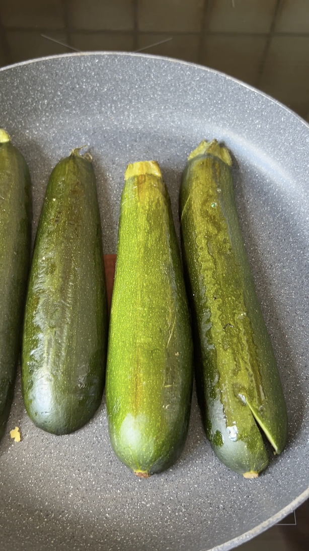 Quatre demies courgettes qui cuisent dans une grande poêle.