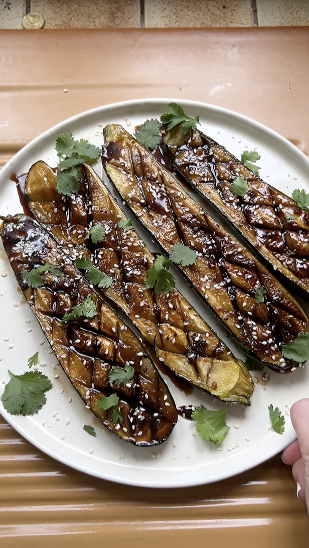 Four zucchini halves on a white plate, with sesame seeds and fresh cilantro.