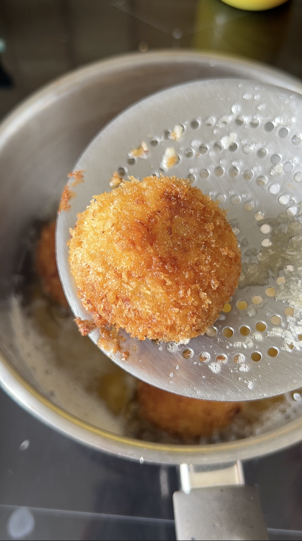 A skimmer pulling a croquetas out of the pan of frying oil.