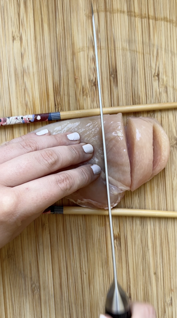 Un couteau qui coupe le filet de poulet, placé entre deux baguettes chinoises.