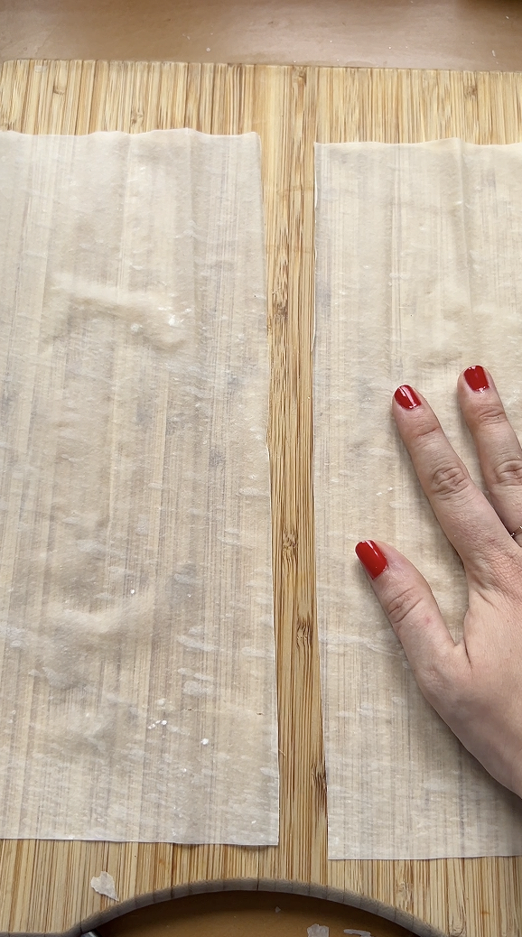 Marie separating two halves of filo pastry sheets on a wooden board.