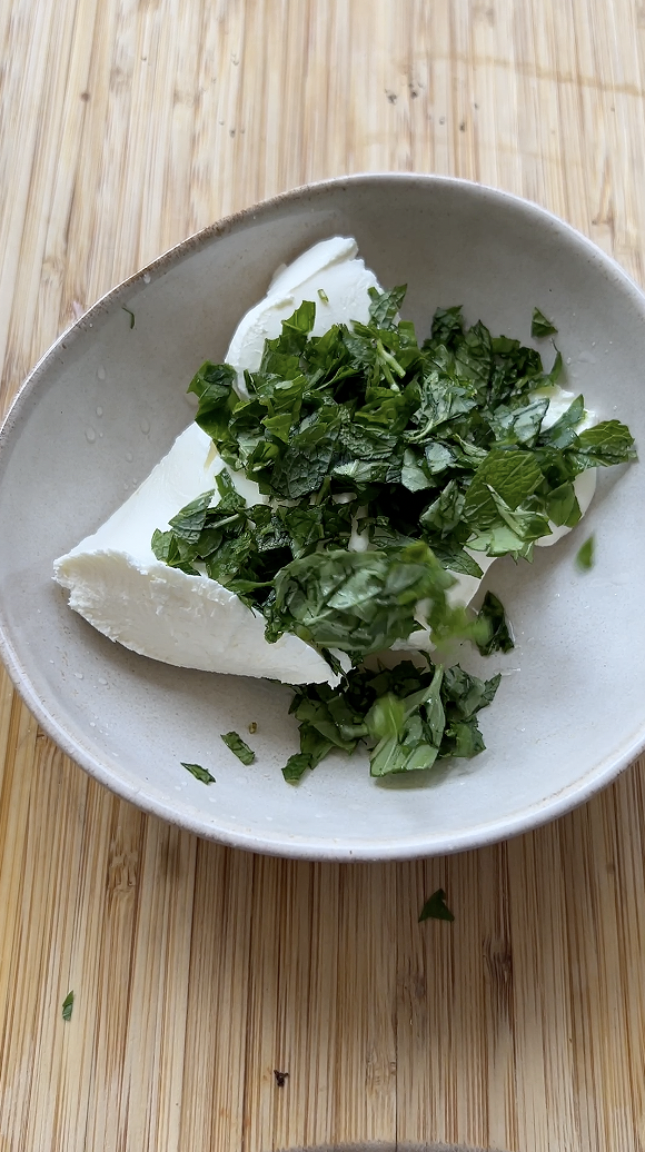 Cream cheese and freshly chopped herbs in a beige bowl.