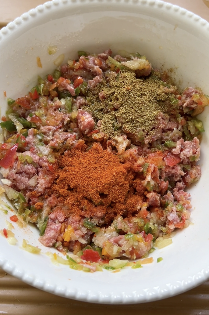 Tomato paste, ground beef, paprika, cumin, parsley, onion and garlic added to the large white bowl of vegetables.