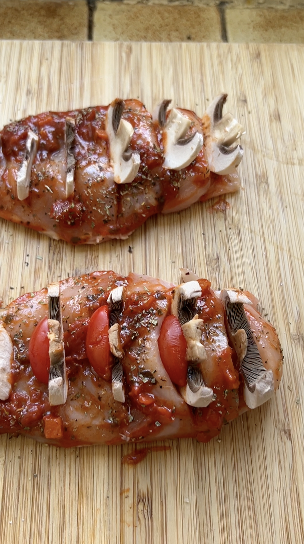 Deux filets de poulet sur une planche en bois, garnis de demies tomates cerises et de lamelles de champignons.