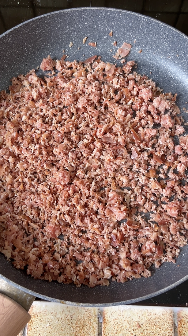 Minced Serrano ham cooking in a large gray frying pan.