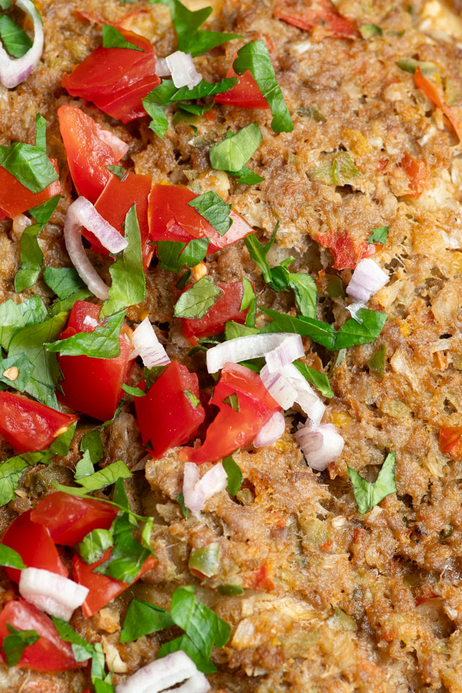 Zoom sur la garniture du Lahmacun avec de la viande, des épices, des morceaux de tomate, des lamelles d'oignon rouge et du persil frais hachés.