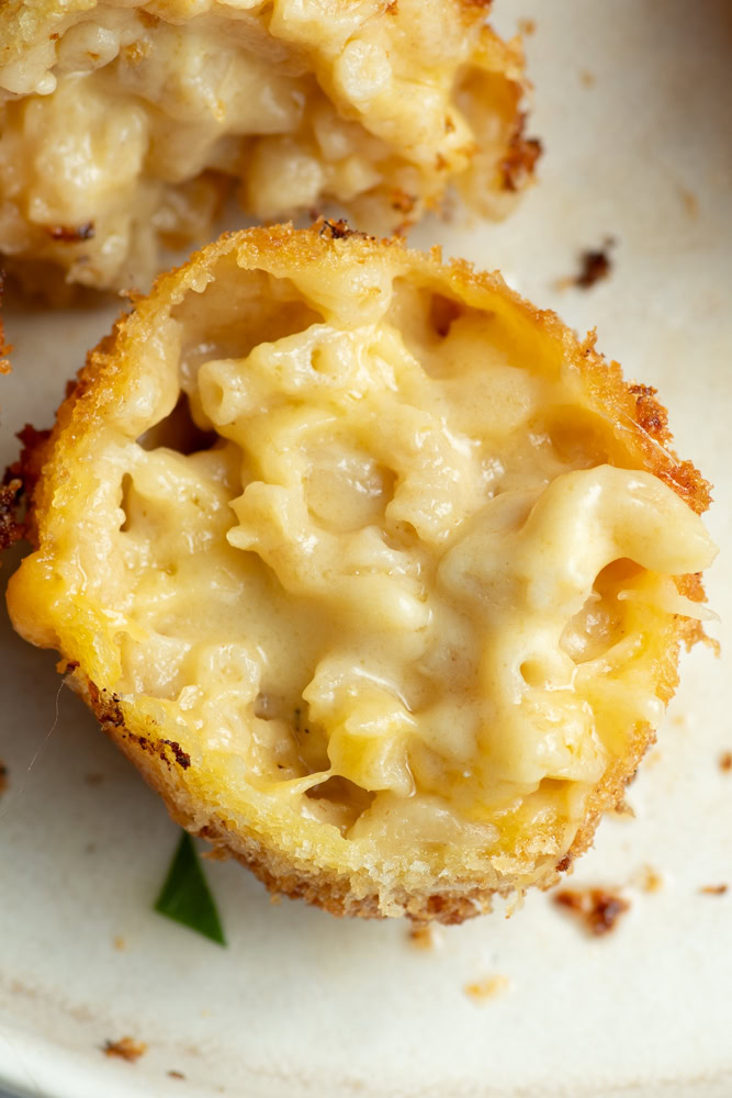 Mac and cheese ball cut in half on a beige plate.