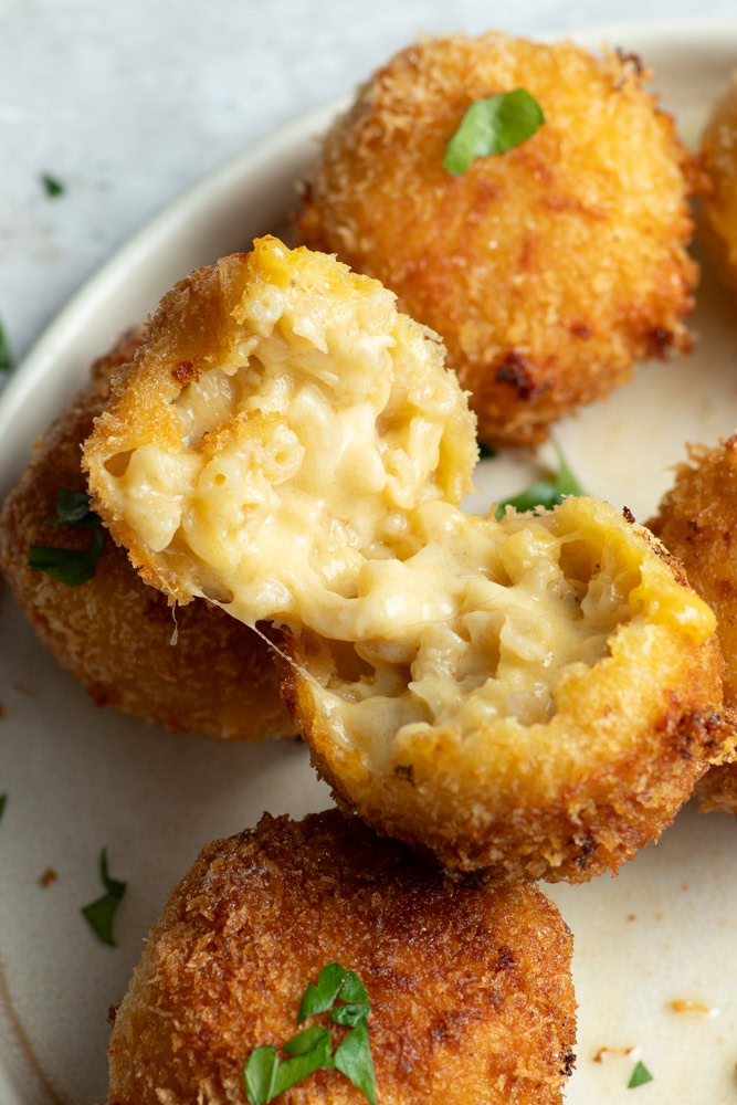 Mac and cheese ball coupée en deux dans une assiette beige, avec d'autres balls.