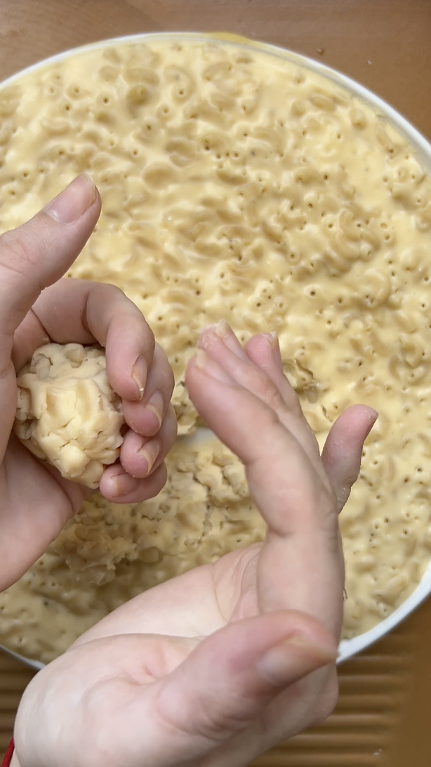 Two hands making Mac and cheese balls.