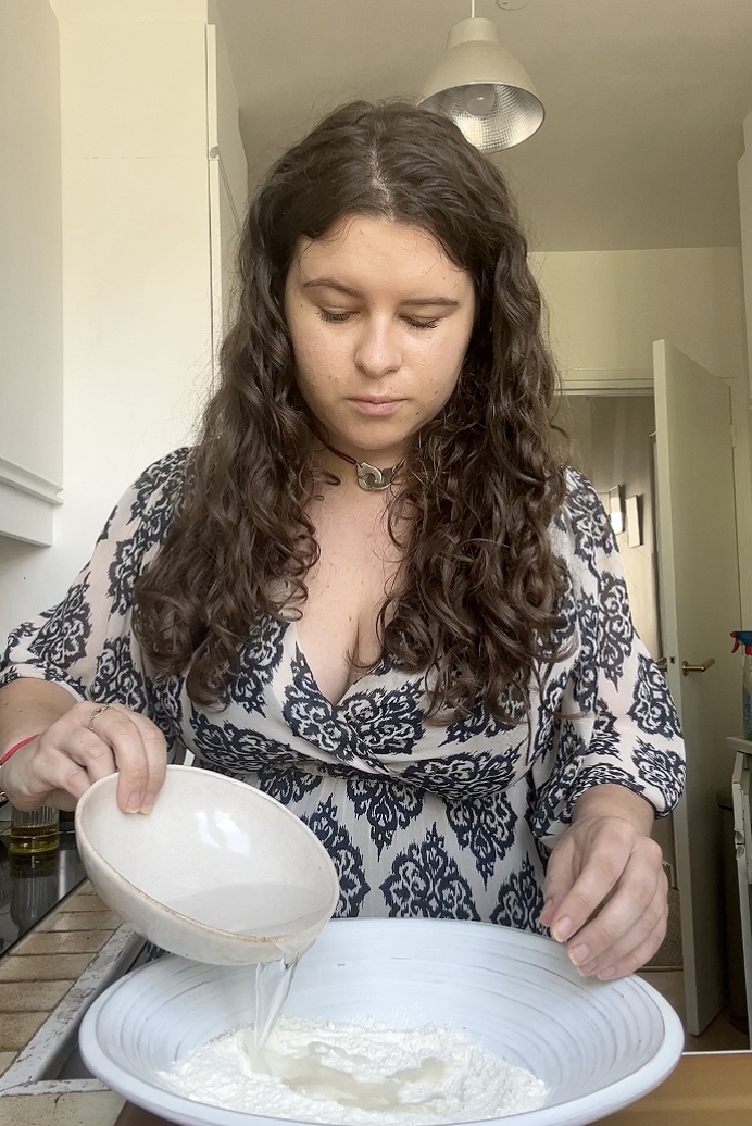 Marie pours a little water into the large bowl of flour.