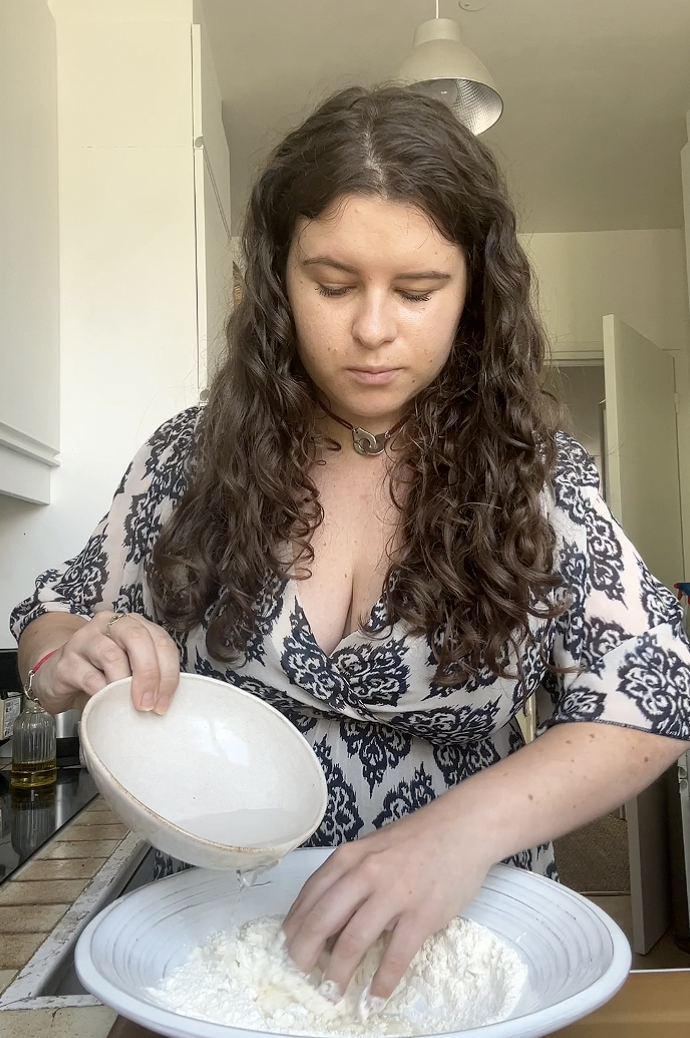 Marie pours a little water into the large bowl of flour.