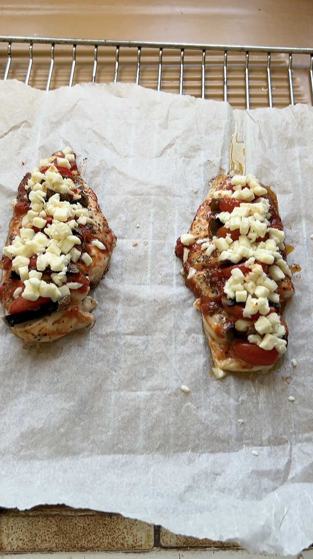 Les deux filets de poulet sur une plaque du four recouverte de papier cuisson recouverts de mozzarella râpée.