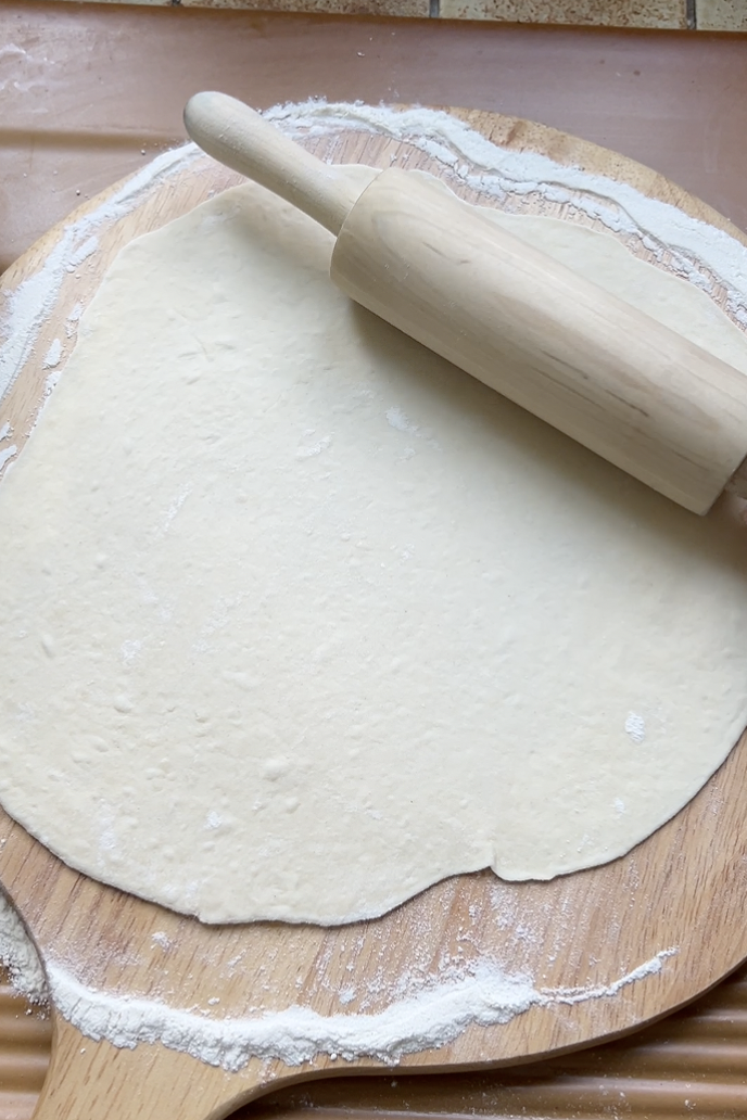 Pâte à Lahmacun abaissée sur une planche ronde avec un rouleau à pâtisserie.