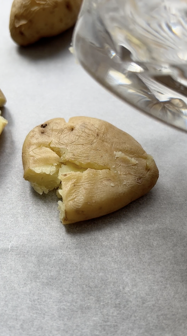 Pomme de terre écrasée par un verre, posée sur une feuille de papier cuisson.