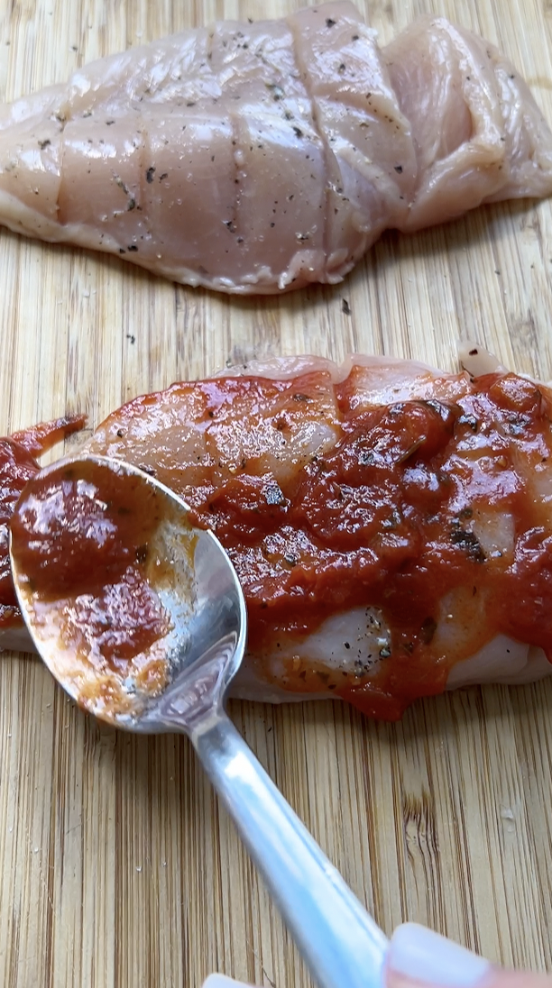 Une cuillère à soupe qui étale de la sauce tomate sur un filet de poulet.