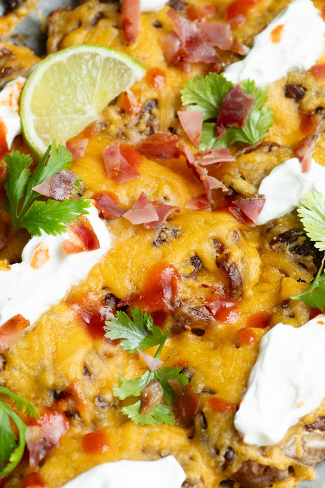 Smashed nacho-style potatoes with lime wedges, fresh cilantro leaves, bacon, Greek yoghurt and spicy sauce.